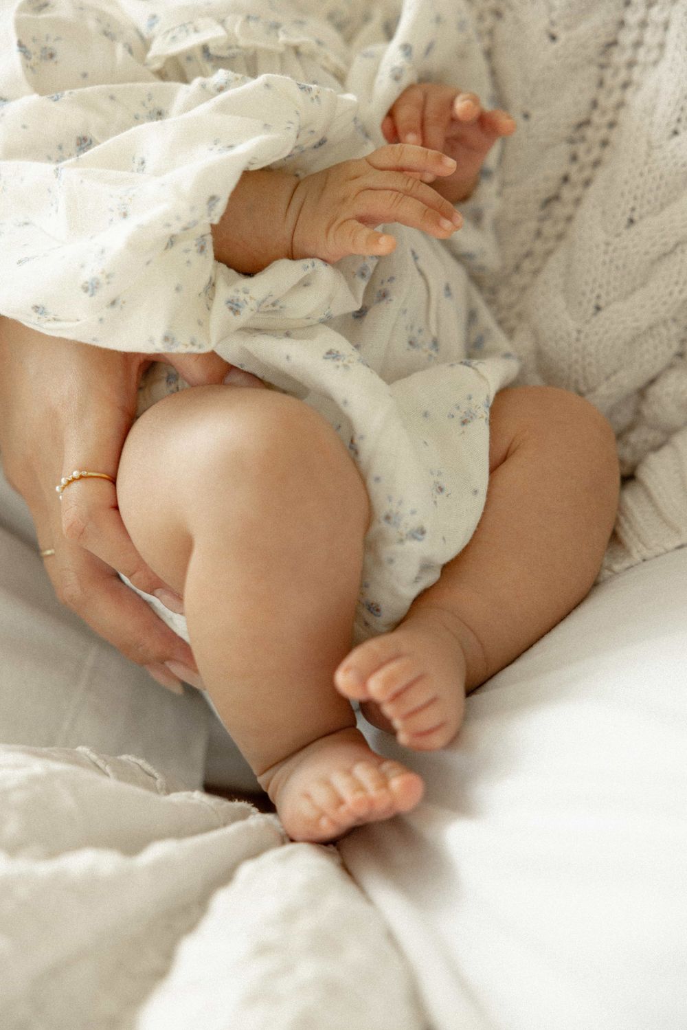 Close-up of newborn baby legs and tiny hands held by mother wearing gold rings.