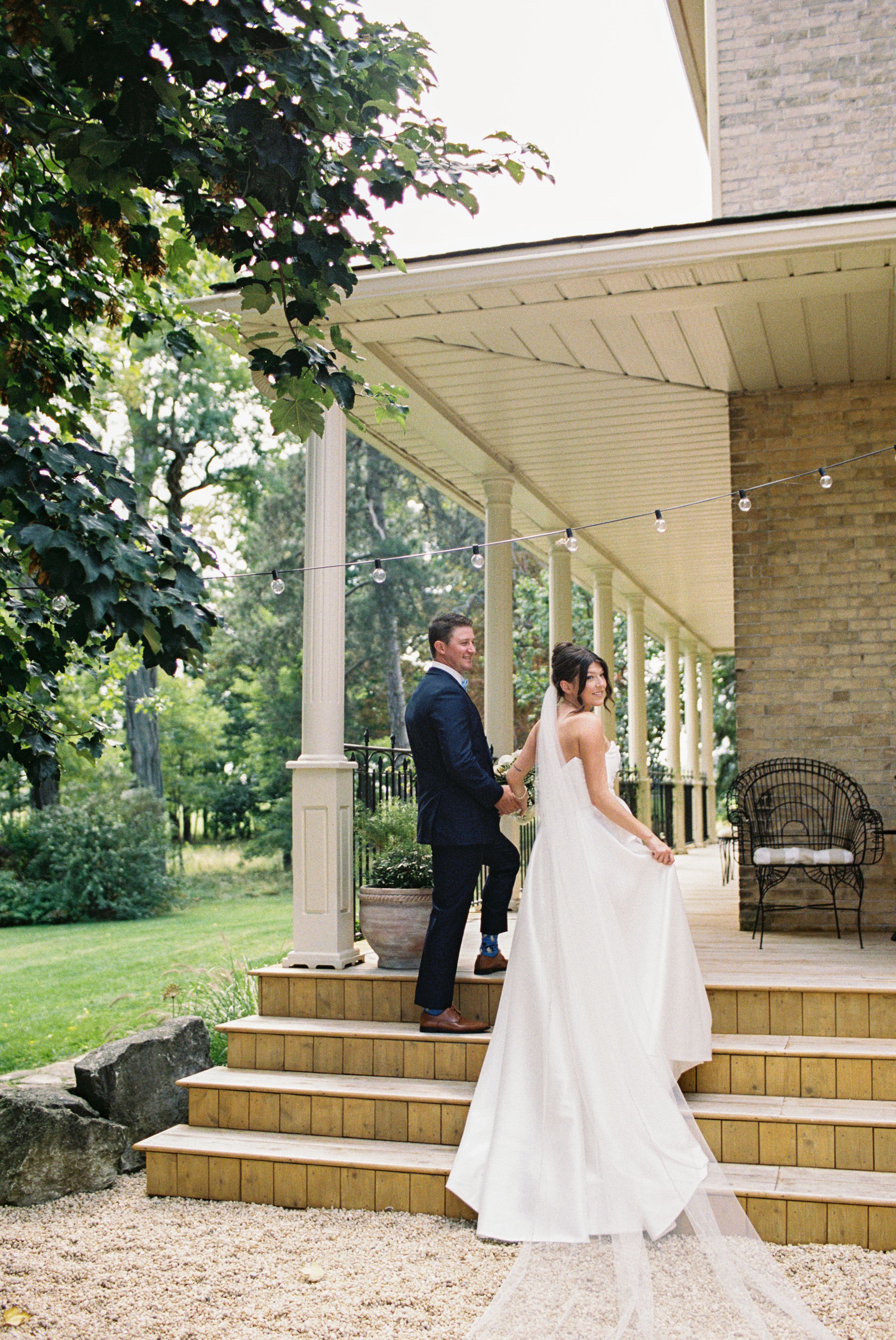 Bride and groom share a tender first look moment on the steps of a charming porch surrounded by lush greenery.
