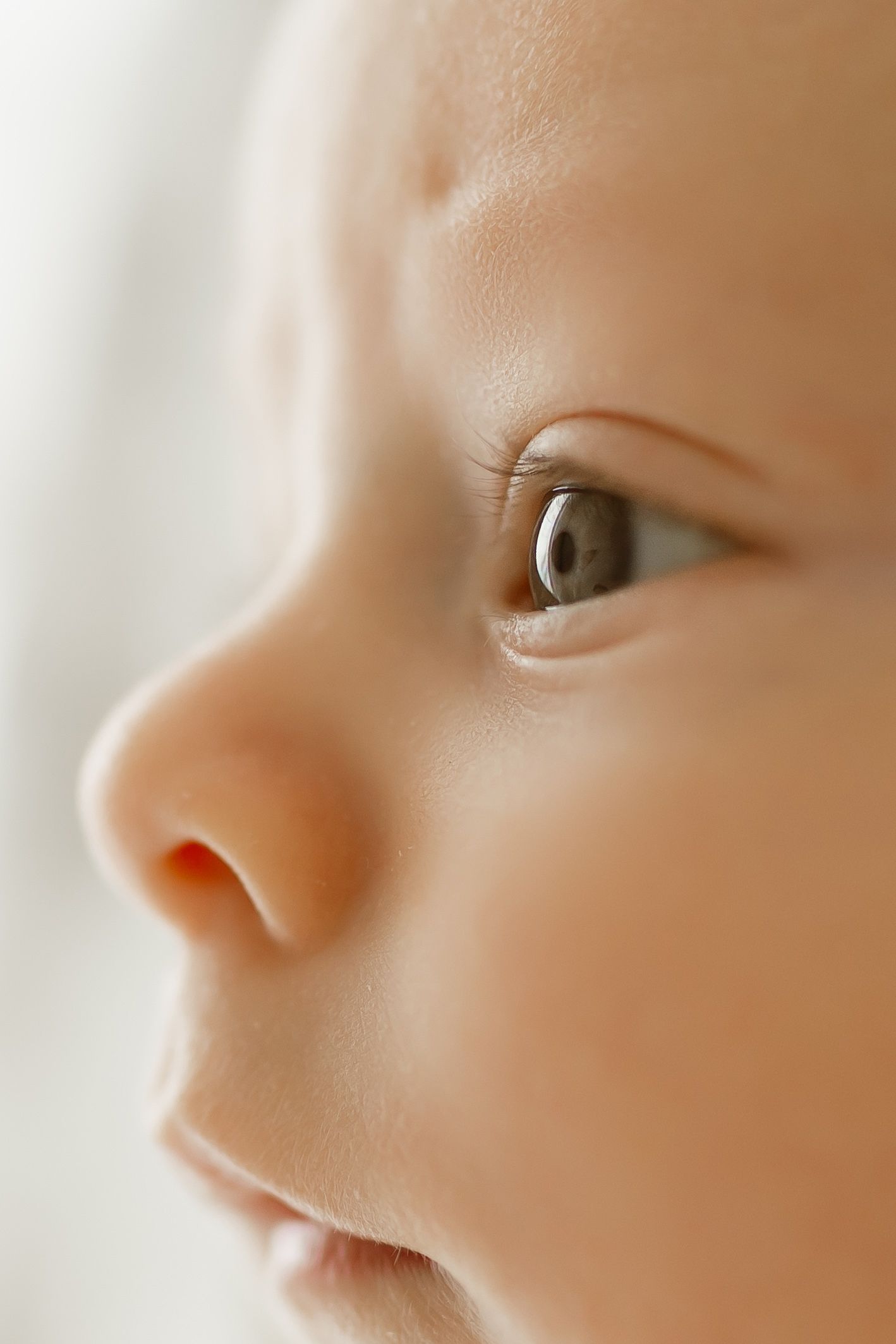 Close-up portrait of a curious baby's face with soft skin, bright eyes, and delicate features in natural light.