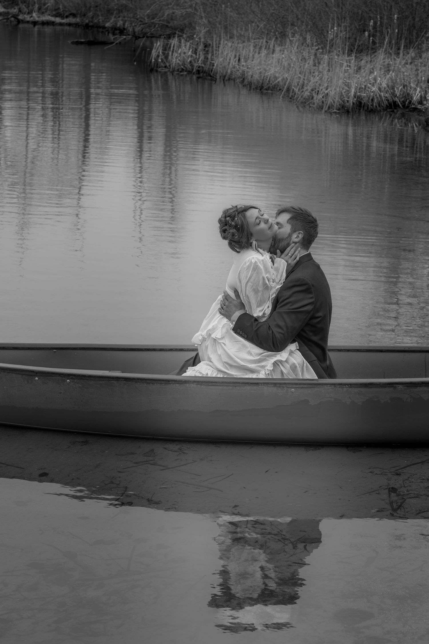 Bride and groom sharing a romantic moment in a teal canoe on a calm lake with forested shoreline.