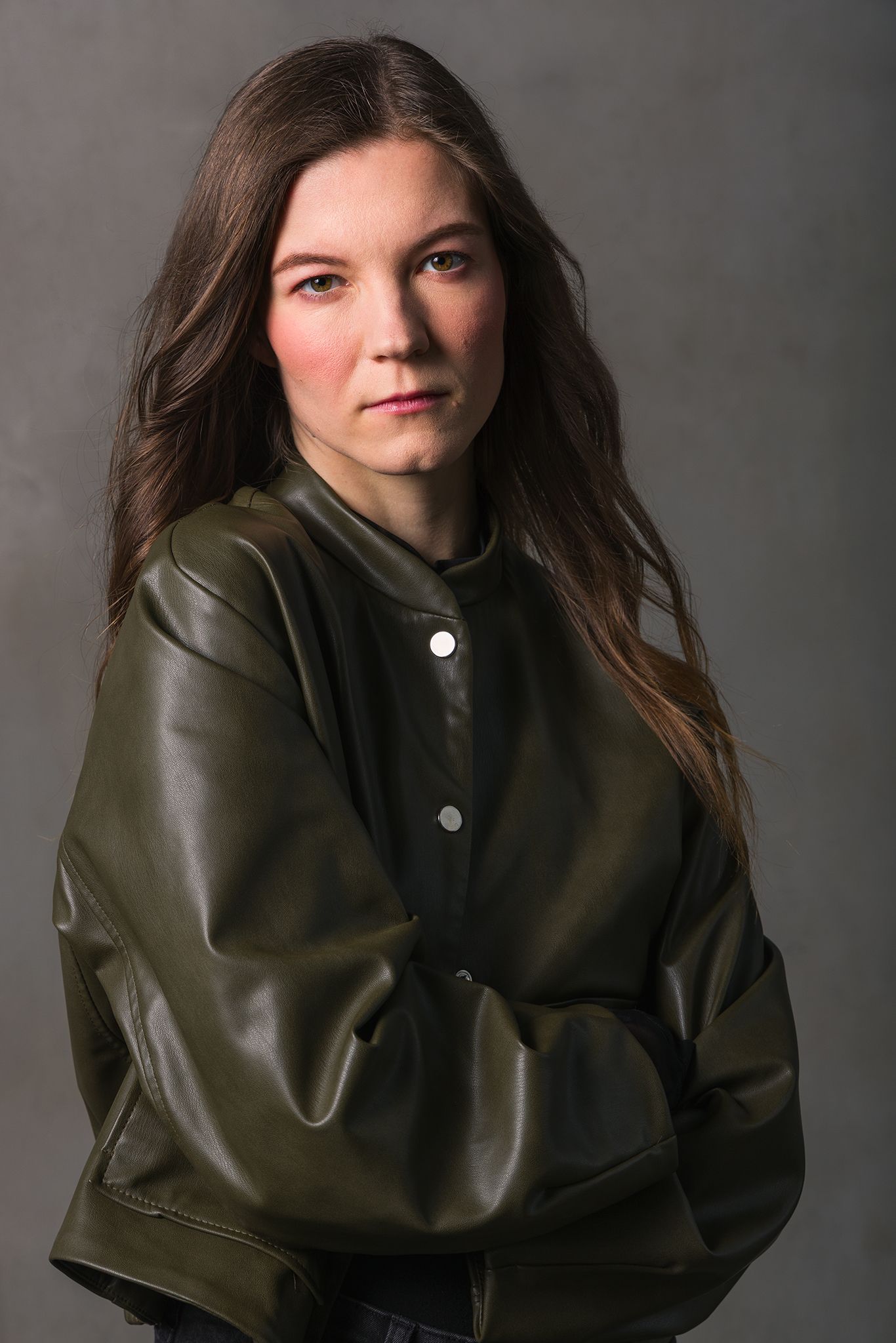 Headshot for filmmaker and photographer, a young woman in an olive green jacket, hair gently flowing behind her.