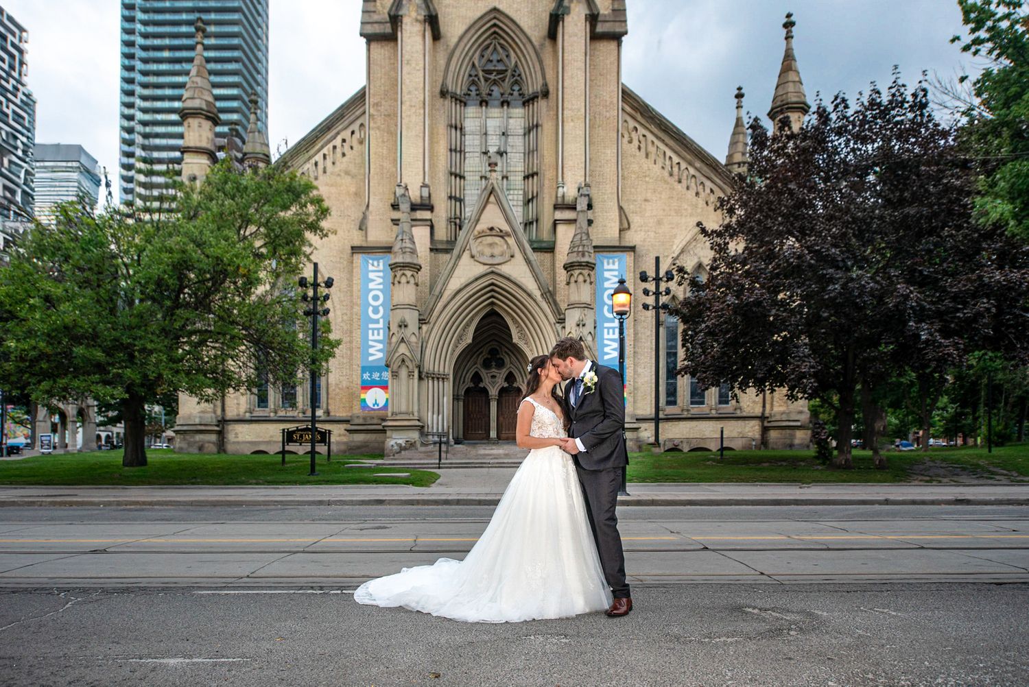 Bride and groom share a romantic kiss outside a majestic Gothic church on their wedding day.