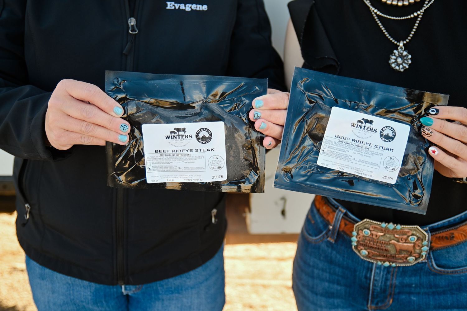 Two people holding packaged Wild West Jerky products outdoors, showcasing artisan meat snacks in dark packaging.