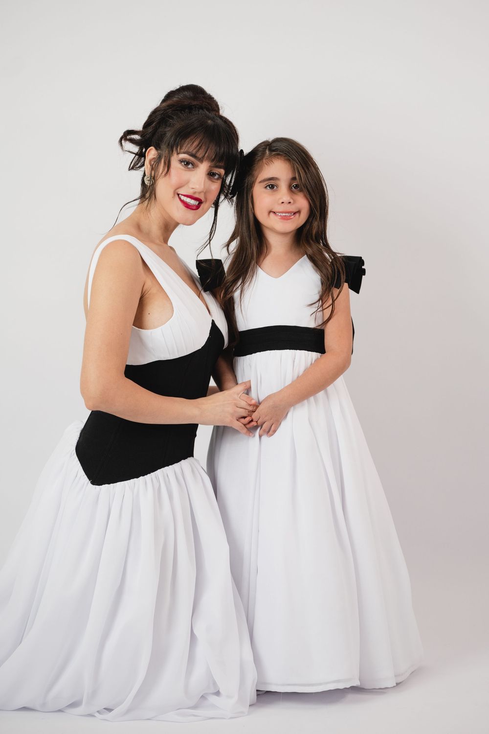 Woman and girl in matching black and white dresses posing together in a studio setting.