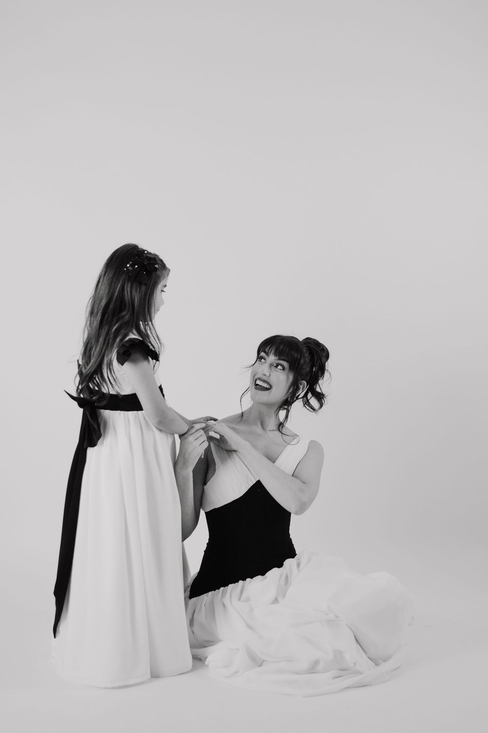Black and white photo of a woman kneeling holding hands with a young girl, both wearing elegant dresses.