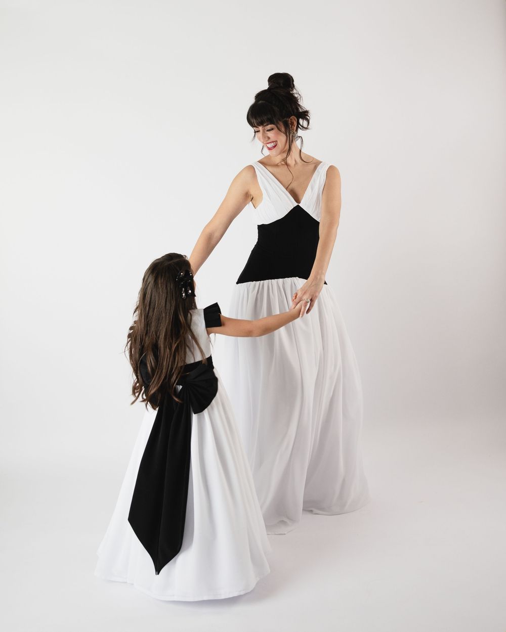 Woman and girl in matching black and white gowns pose together in a studio setting.