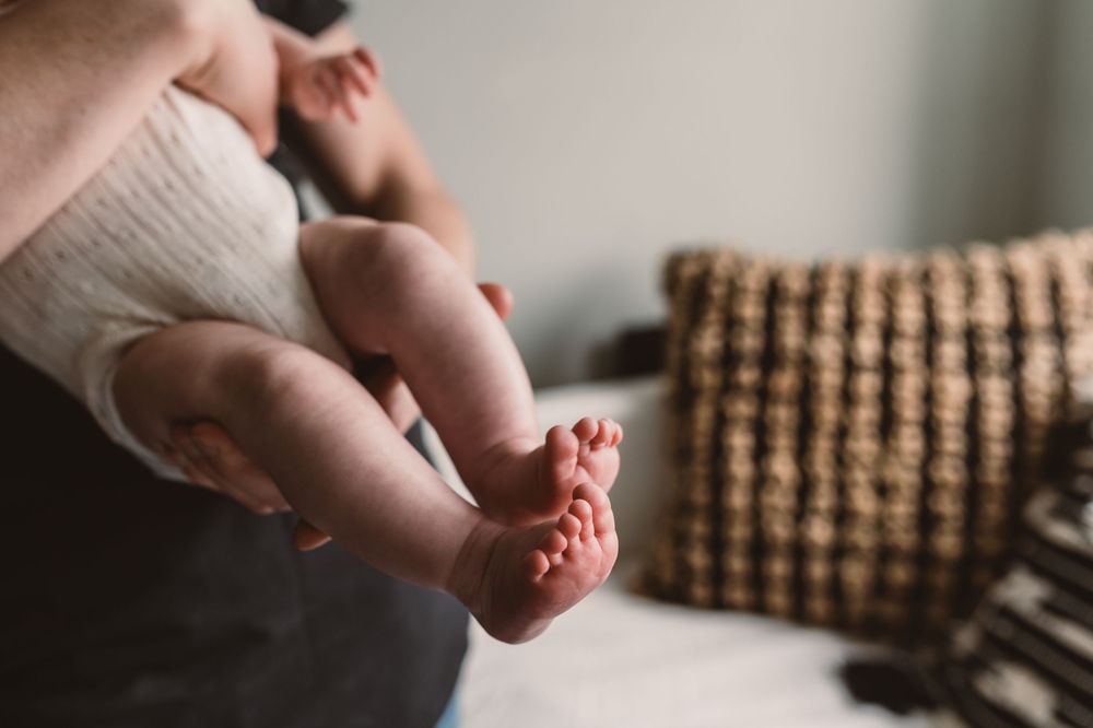 Close-up of a newborn baby's tiny feet being held by a parent in a softly lit room.