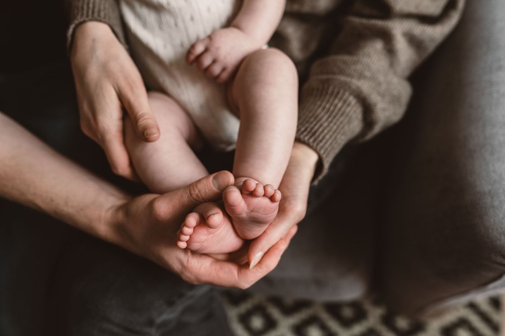 Adult hands gently cradling tiny newborn baby feet, capturing a tender parent and infant bonding moment.