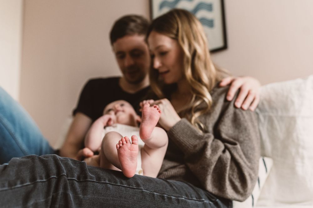 A couple lovingly gazes at their newborn baby, focusing on the infant's tiny feet in a cozy home setting.
