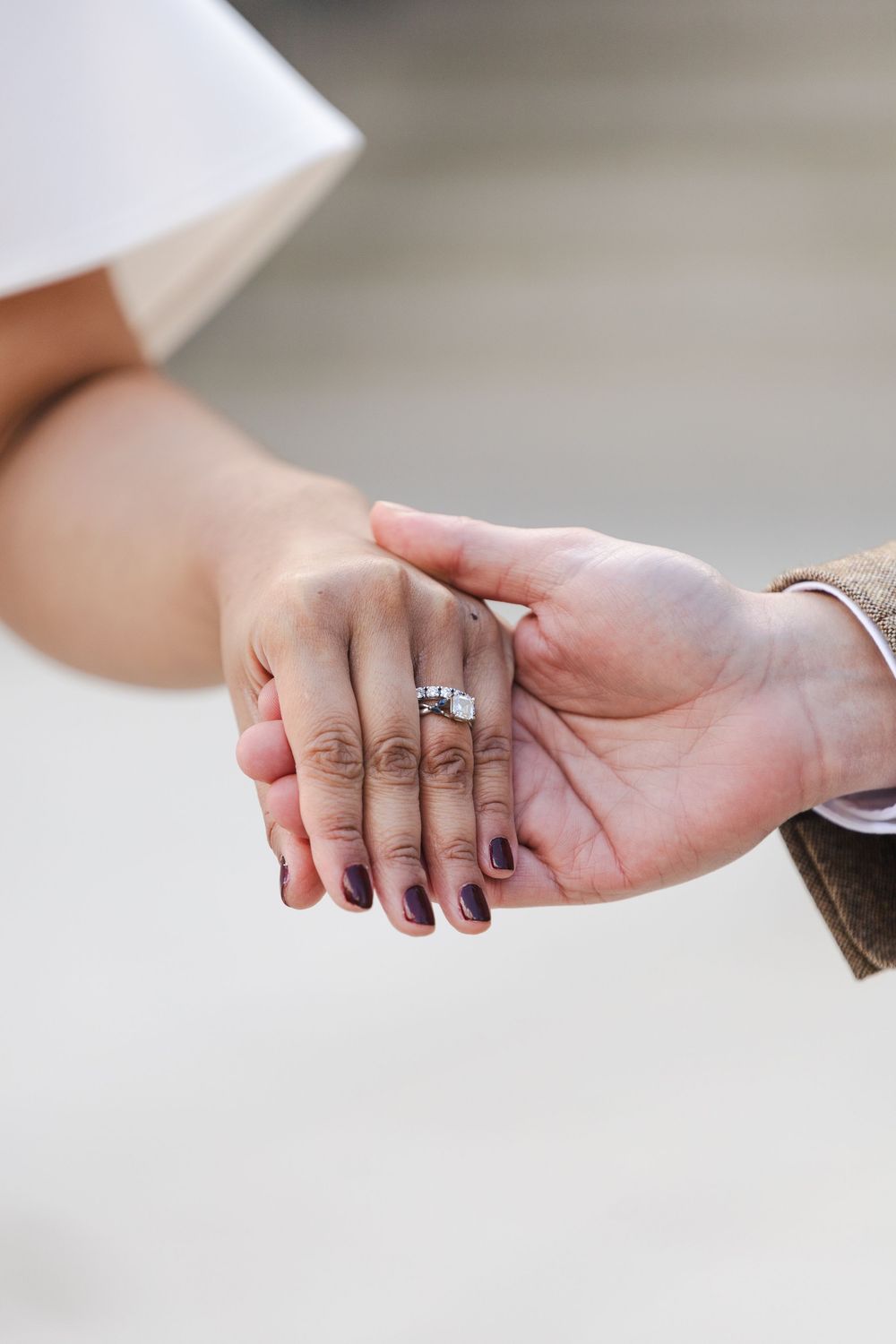 Close-up of a couple holding hands, showcasing a diamond engagement ring on the bride's finger with dark nail polish.