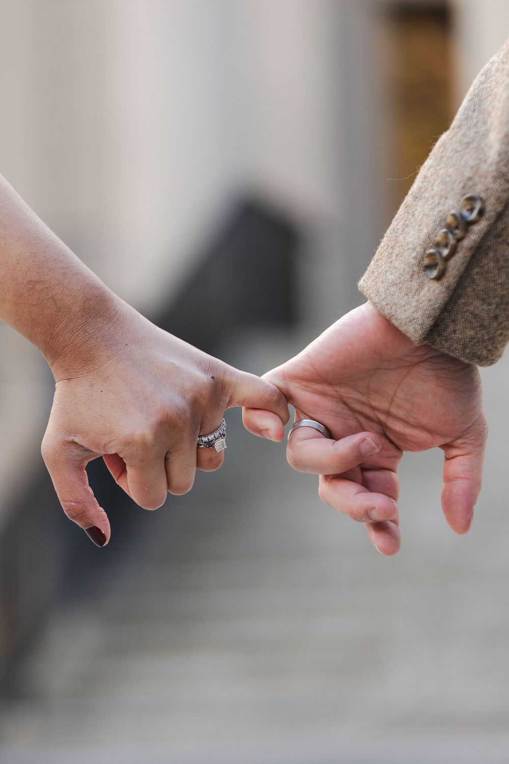 Two hands with wedding rings linked by pinky fingers, symbolizing love and commitment.