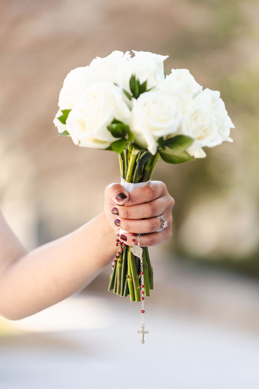 Hand holding white rose bouquet with rosary beads and cross pendant, perfect for a wedding or religious ceremony.