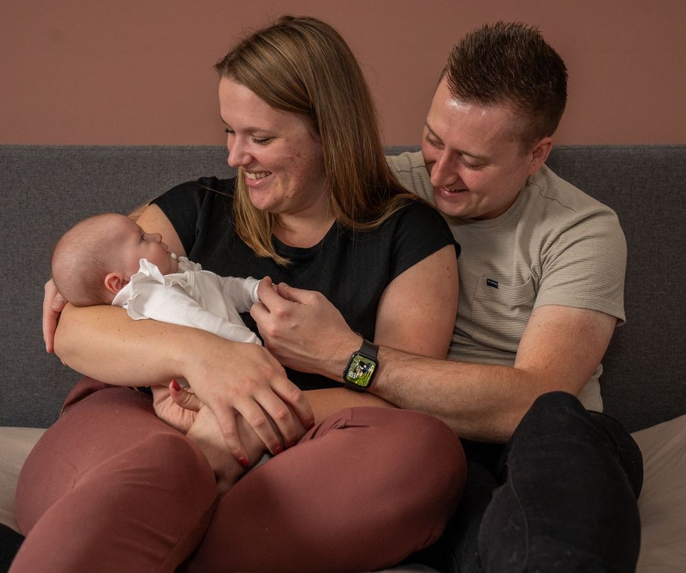 Een gelukkig stel zit lachend op de bank terwijl ze hun pasgeboren baby thuis vasthouden.