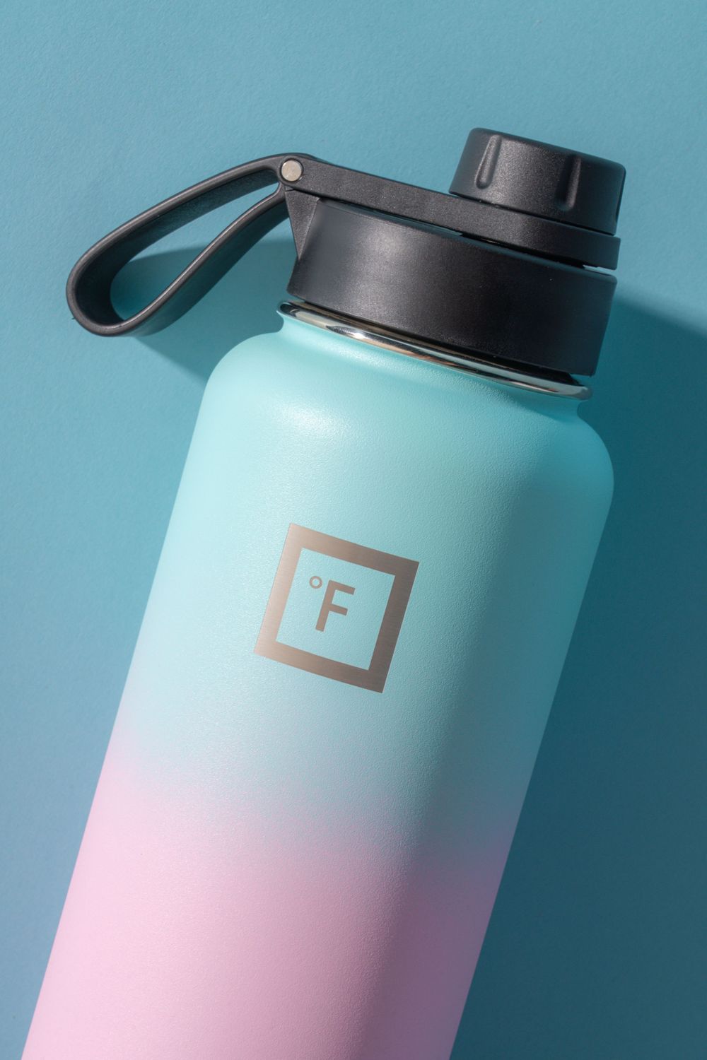 Close-up of gradient mint and pink water bottle with black lid against blue background.