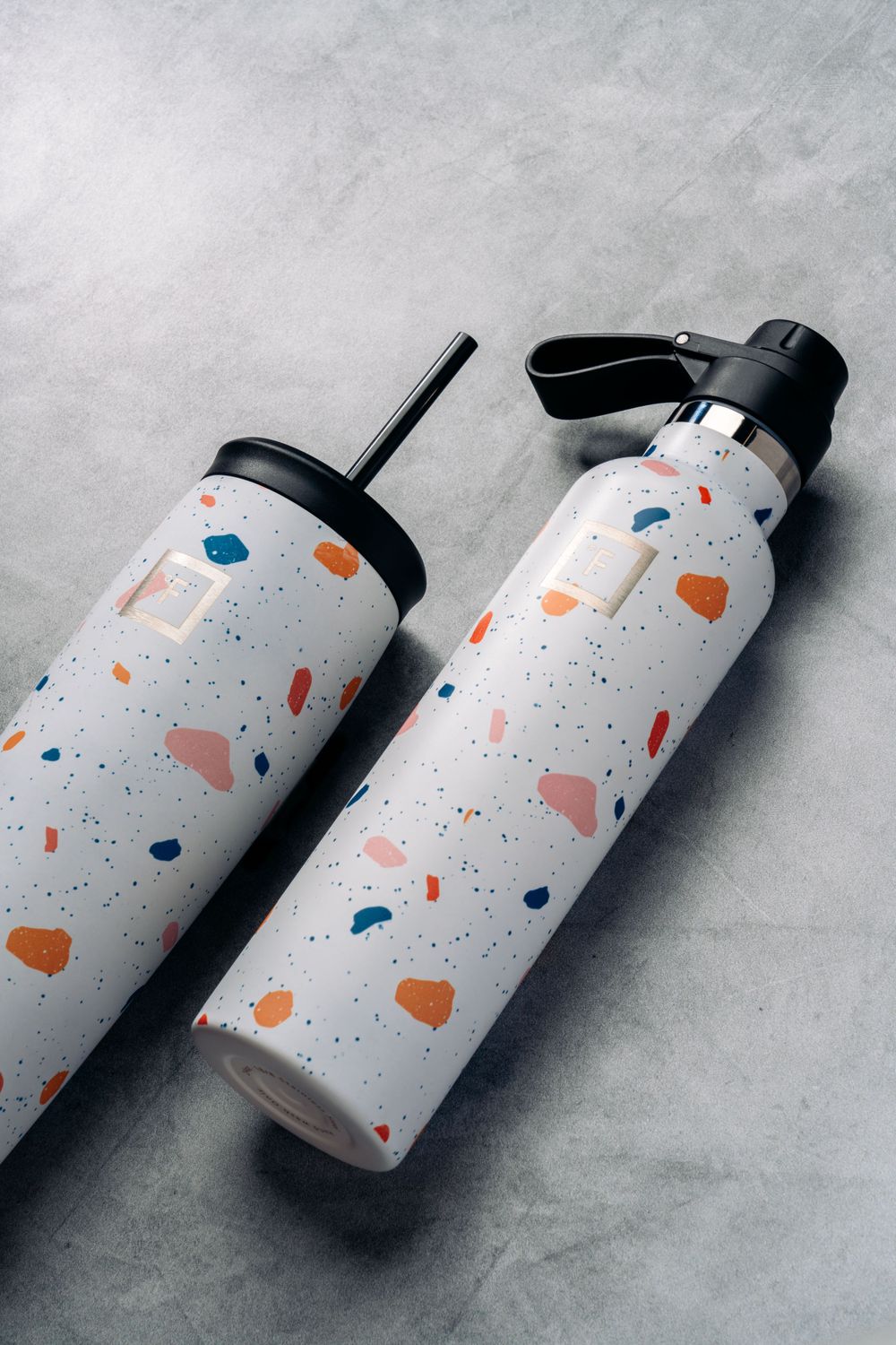 Two terrazzo-patterned insulated water bottles with straw lids on gray background.