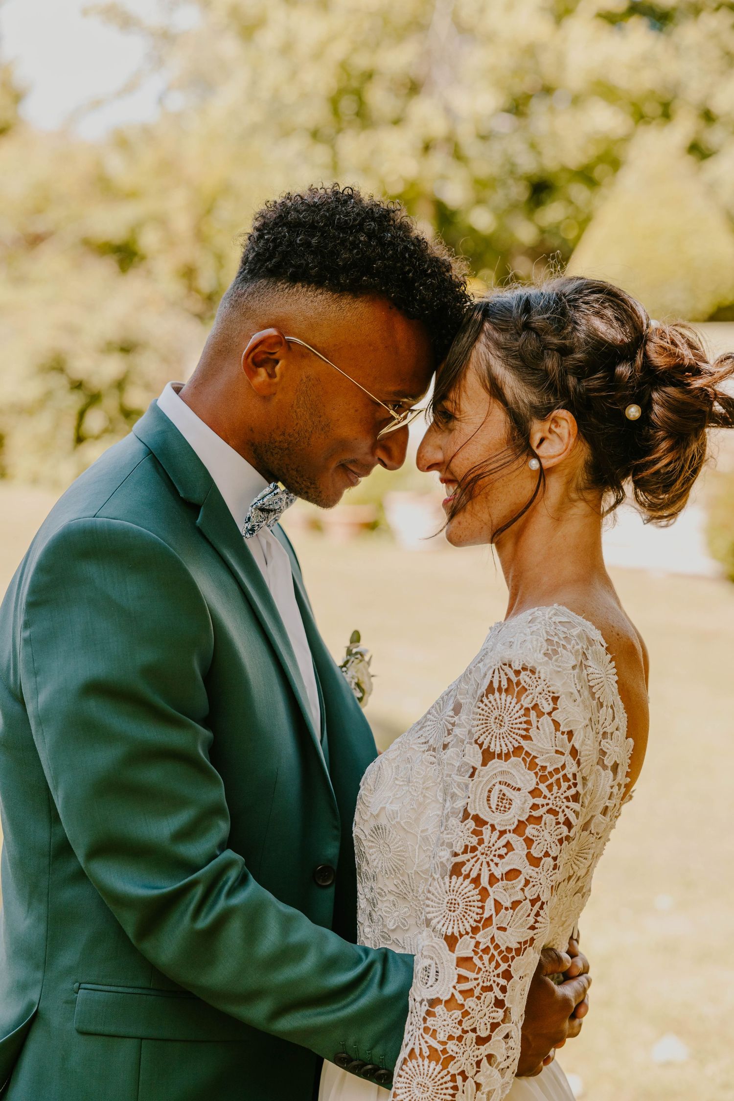 A bride and groom hold hands outside a historic stone church, she in a white gown holding a bouquet, he in a cream suit.