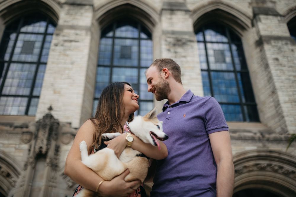Couple smiling at each other while holding a cute Corgi dog in front of a Northwestern University building during engagement session