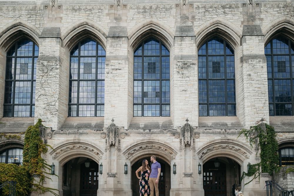 Couple posing in front of grand Gothic stone building of Northwestern University with tall arched windows and ornate architectural details