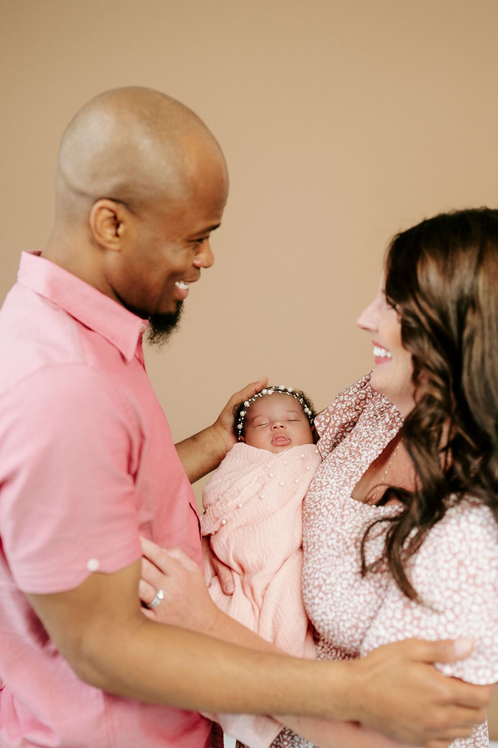 Happy interracial couple smiling at their newborn baby girl wrapped in pink with floral headband.