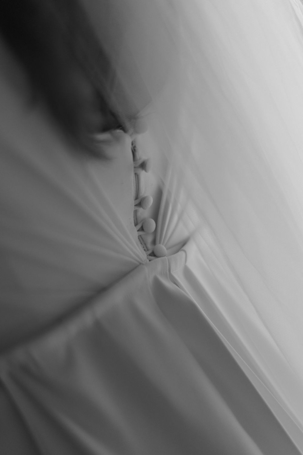 Black and white close-up of a wedding dress back with delicate buttons and flowing fabric details.