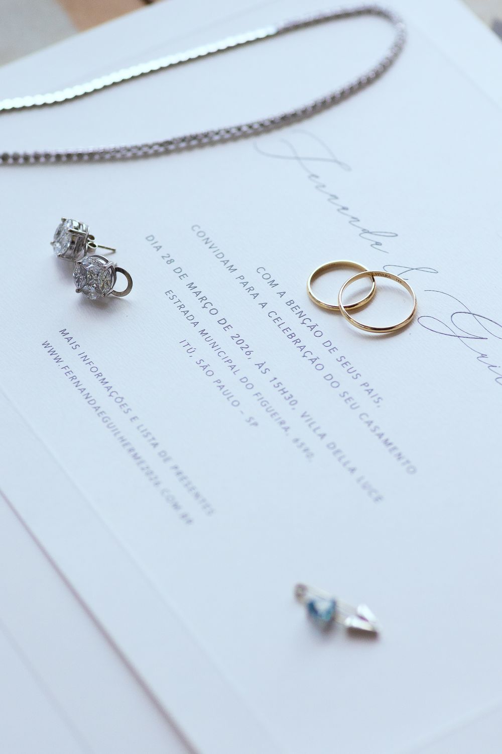 Wedding invitation with gold bands, diamond earrings, and jewelry on white background.