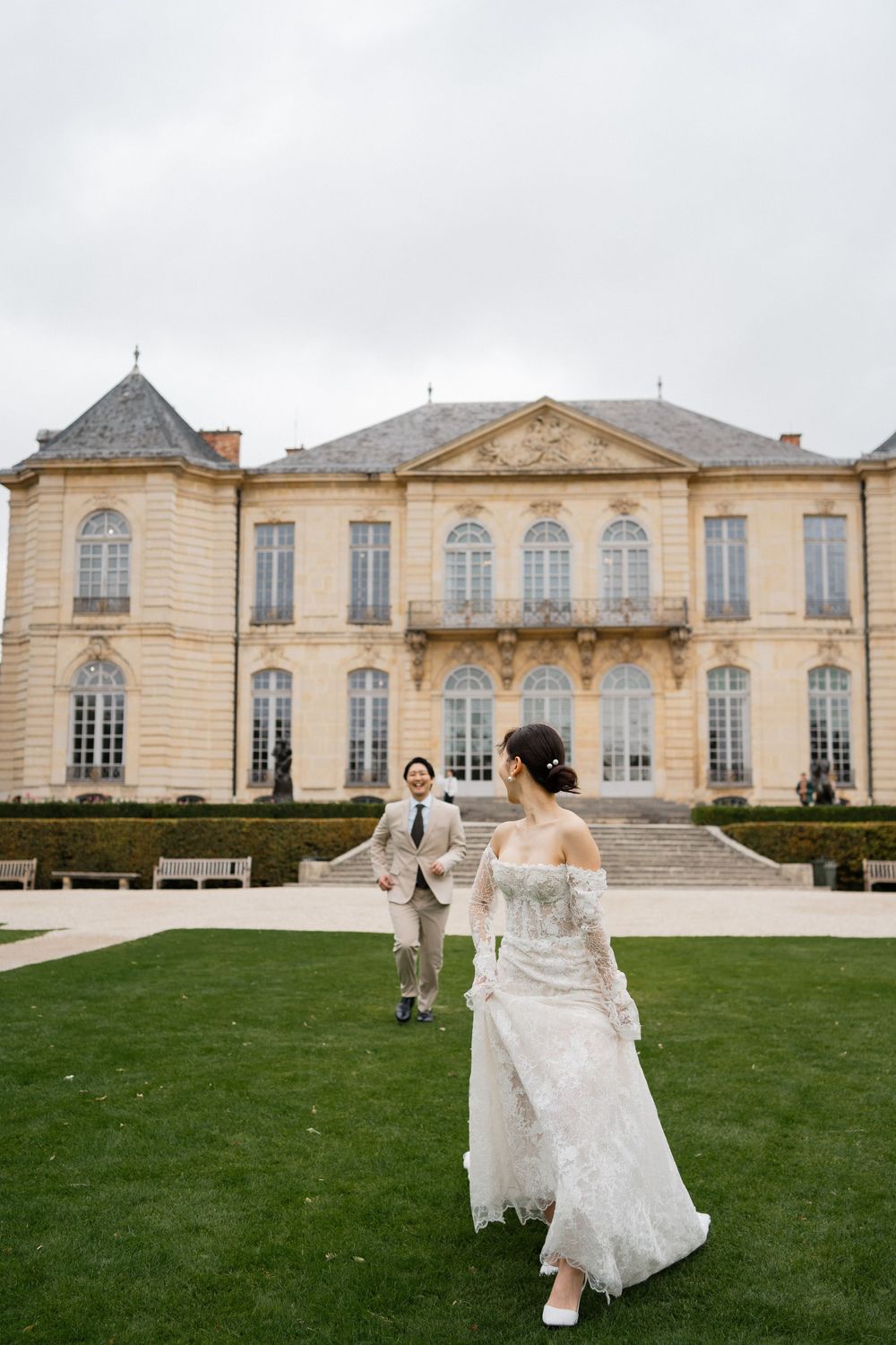 Bride and groom share a romantic moment on lush lawn outside elegant French chateau wedding venue. Paris editorial wedding photos. Film