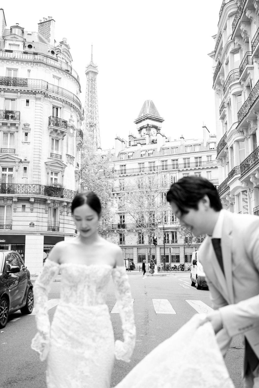 Black and white photo of a couple in wedding attire on a Parisian street with the Eiffel Tower in the background. Paris film photographer