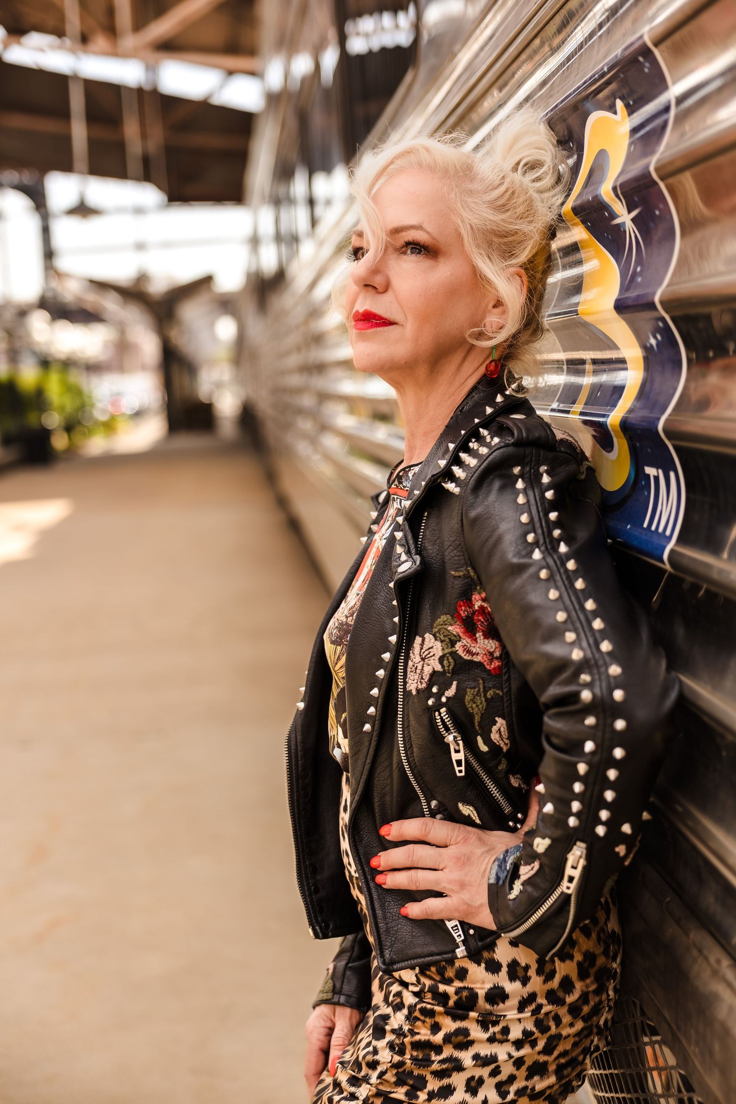 An editorial portrait of a woman in a studded leather jacket posing against a textured, industrial backdrop in Austin, Texas.