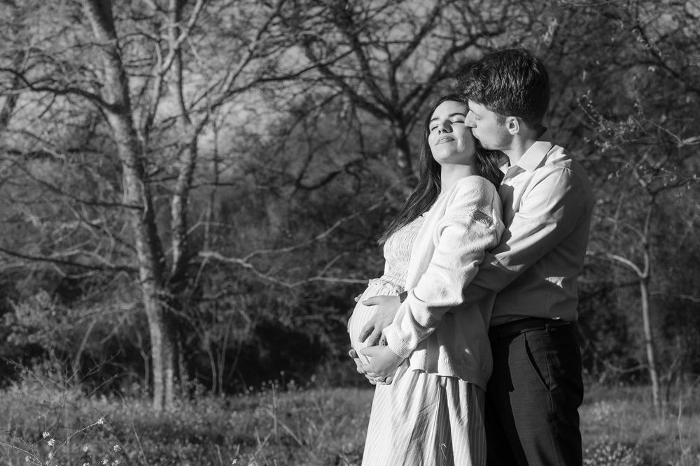 A timeless black and white maternity portrait of a couple leaning against each other in a wooded Buda, Texas setting.