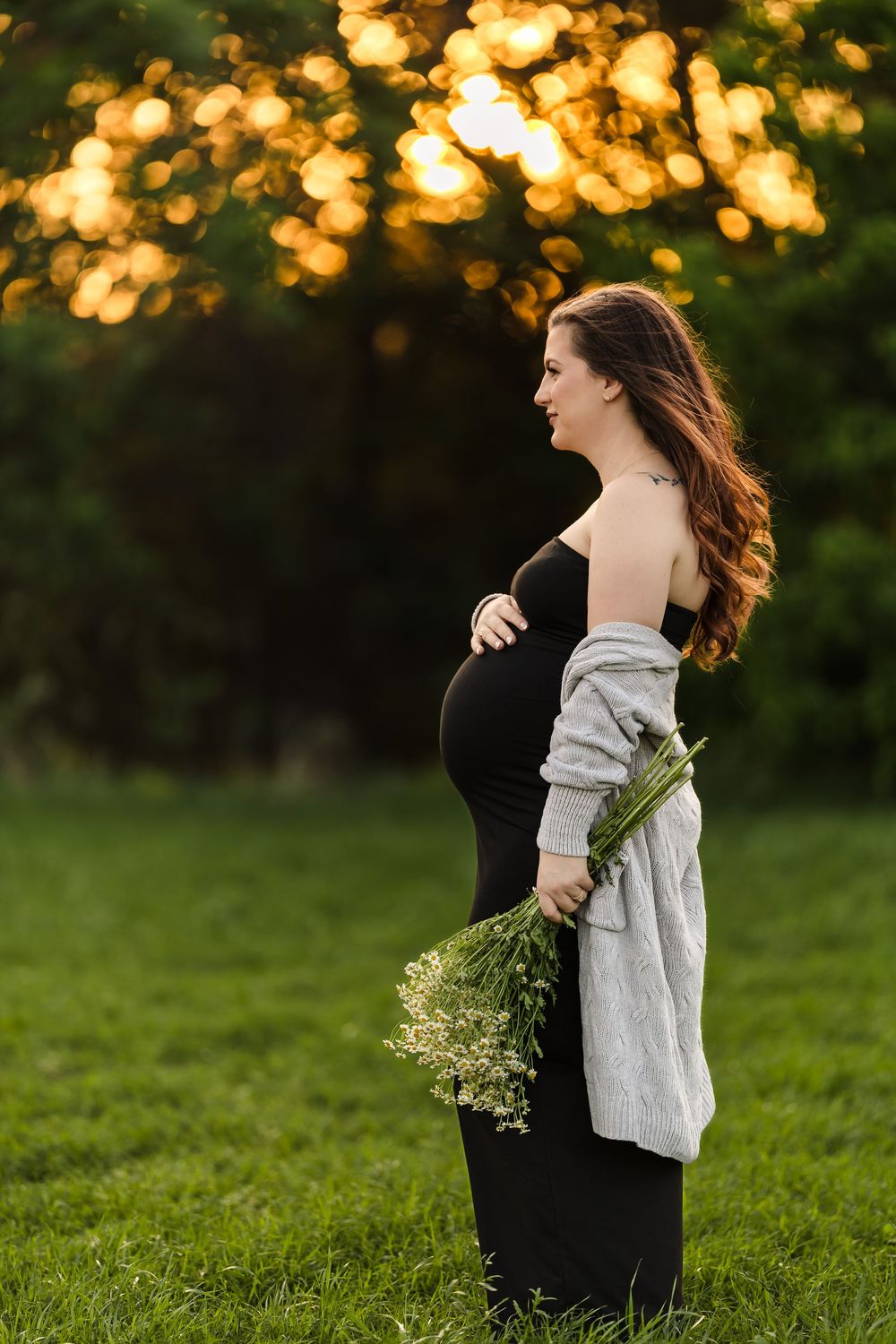A serene maternity session portrait of a woman in a black dress standing in an open field during golden hour in Buda, Texas.