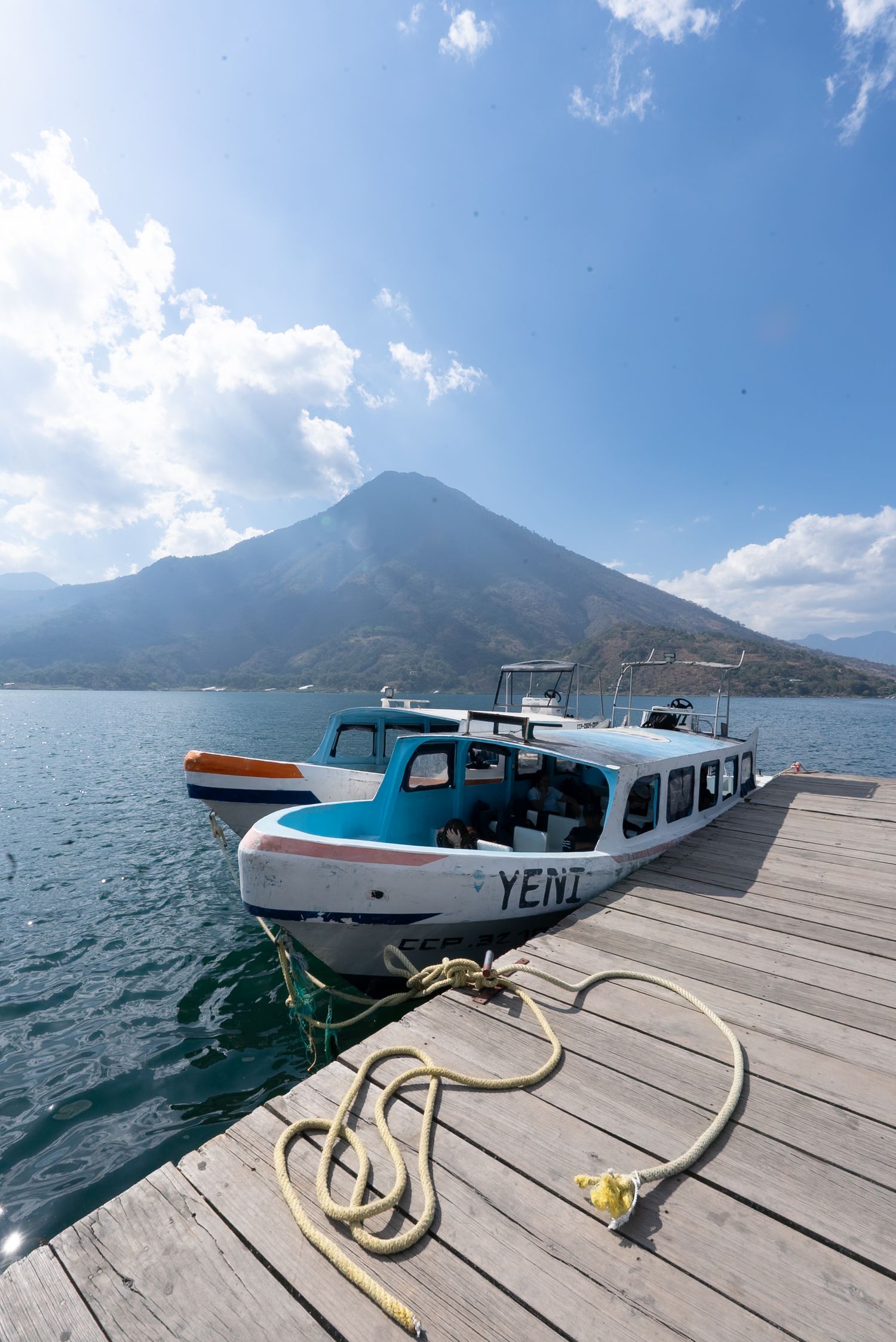 A scenic series of docks and piers extend into Lake Atitlan with a majestic volcano visible in the background.