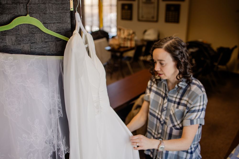 Woman in plaid shirt examining a white wedding dress hanging on a green hanger in a bridal shop.