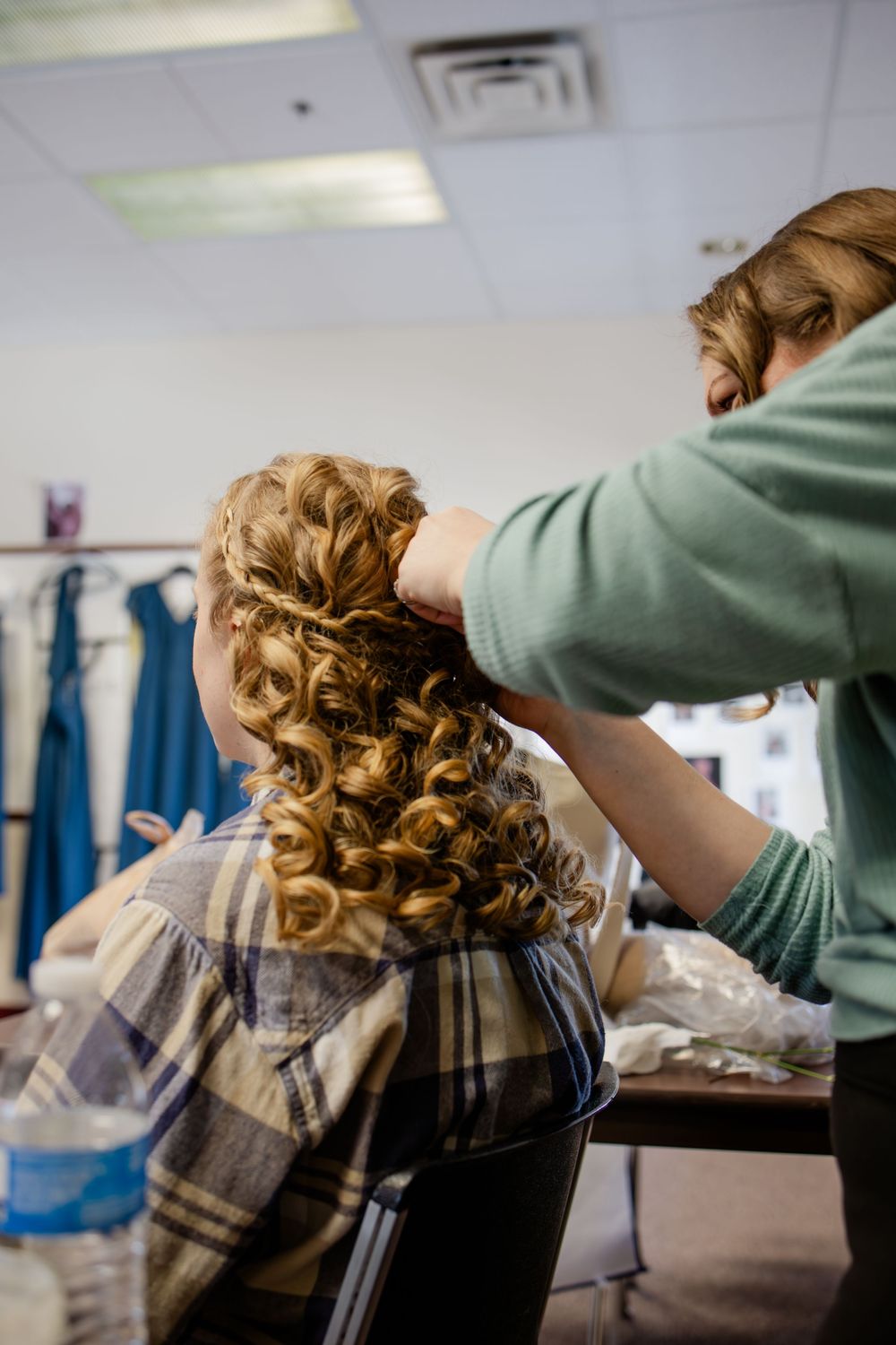 Hairstylist curling and styling a bride's long auburn hair into elegant ringlets before a wedding ceremony.