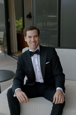 Professional headshots and portraits of someone in a classic black tuxedo sitting by a window in natural light.