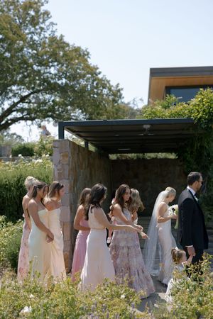 Wedding party in pastel dresses walking together along a garden path.
