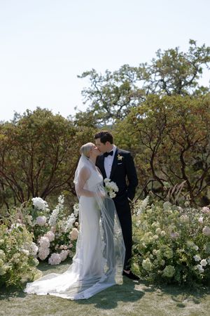 A couple shares an intimate moment among blooming white flowers in a garden wedding setting.