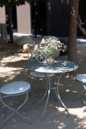 White metal outdoor cafe tables with delicate flower arrangements cast dappled shadows in a garden setting.