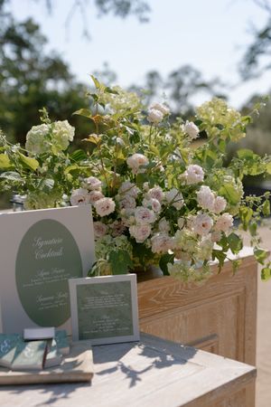 Wooden planter boxes with delicate pink roses and green signage create an elegant outdoor wedding display.