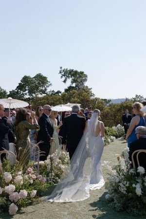 Outdoor wedding ceremony with floral arrangements lining the aisle under a bright blue sky.