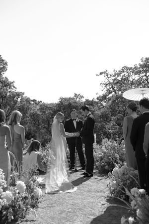 Black and white photograph of wedding guests gathered for an outdoor ceremony with floral decorations.