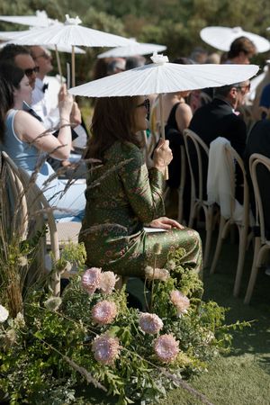 Outdoor wedding ceremony setup with white parasols and pink floral arrangements lining the aisle.
