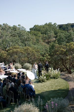 Wedding ceremony guests seated in rows on a grassy hillside surrounded by trees.