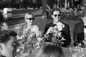 Black and white photograph showing a festive outdoor wedding reception with floral centerpieces and guests seated at tables.