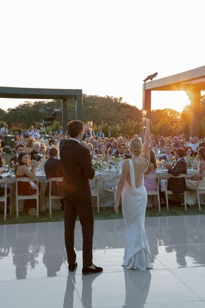 Couple dancing at an outdoor wedding reception on a white dance floor as the sun sets behind them.