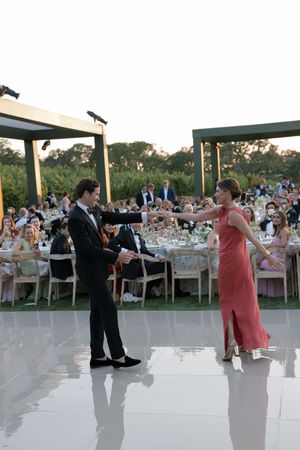 People dancing at an elegant outdoor wedding reception on a white dance floor during sunset.