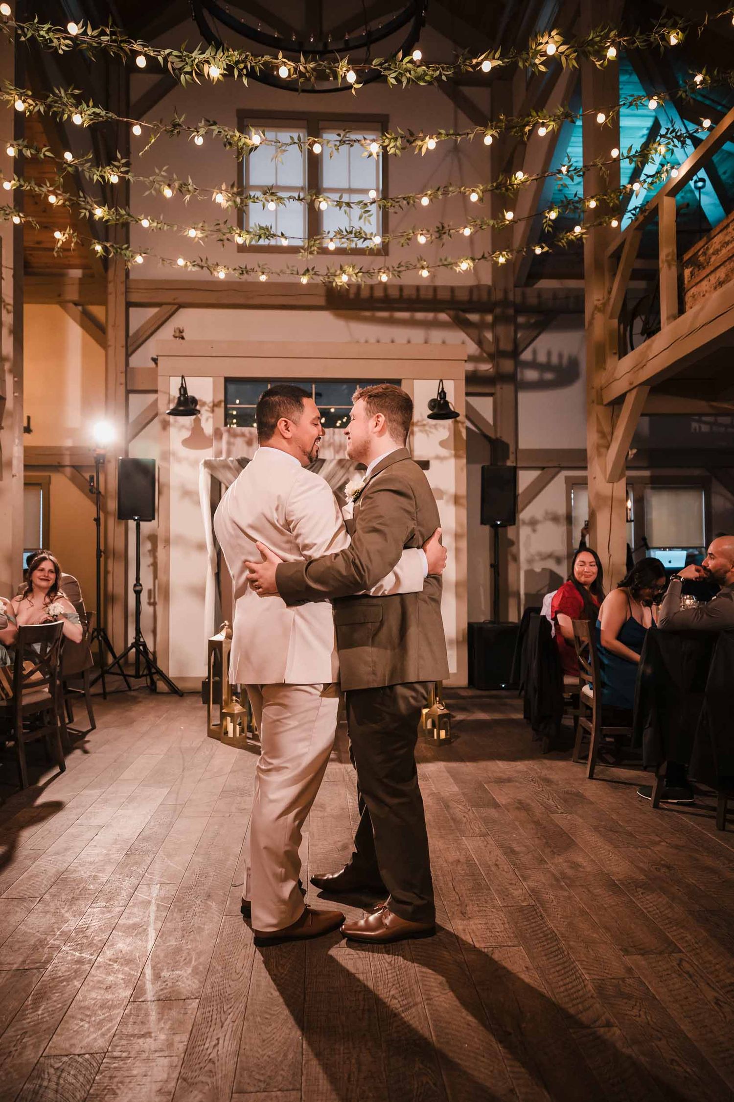 Grooms sharing their first dance under string lights at Briar Barn Inn wedding reception