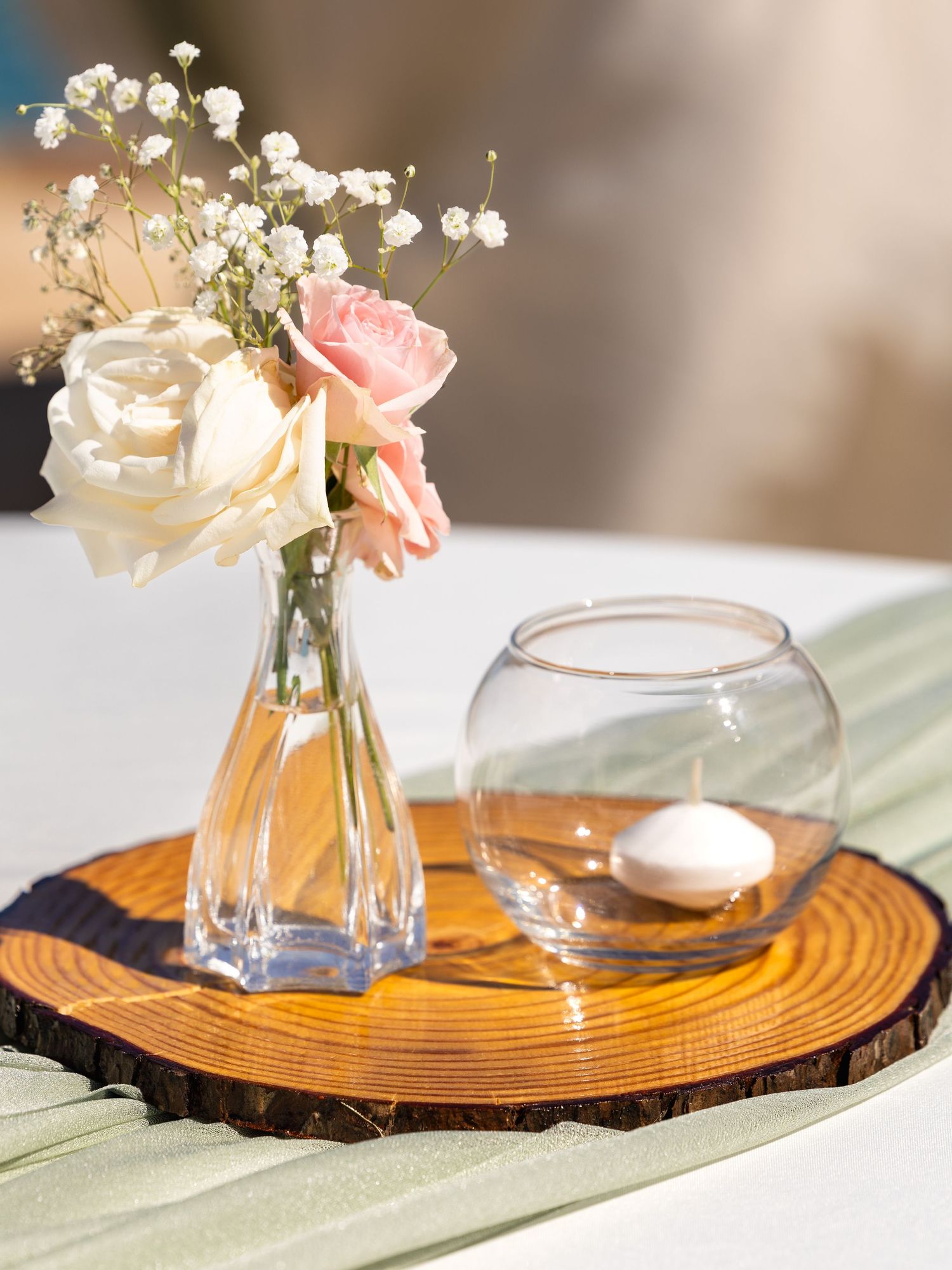 A delicate wedding centerpiece with white roses and baby's breath in a glass vase on a rustic wood slice at an Austin, Texas wedding venue.