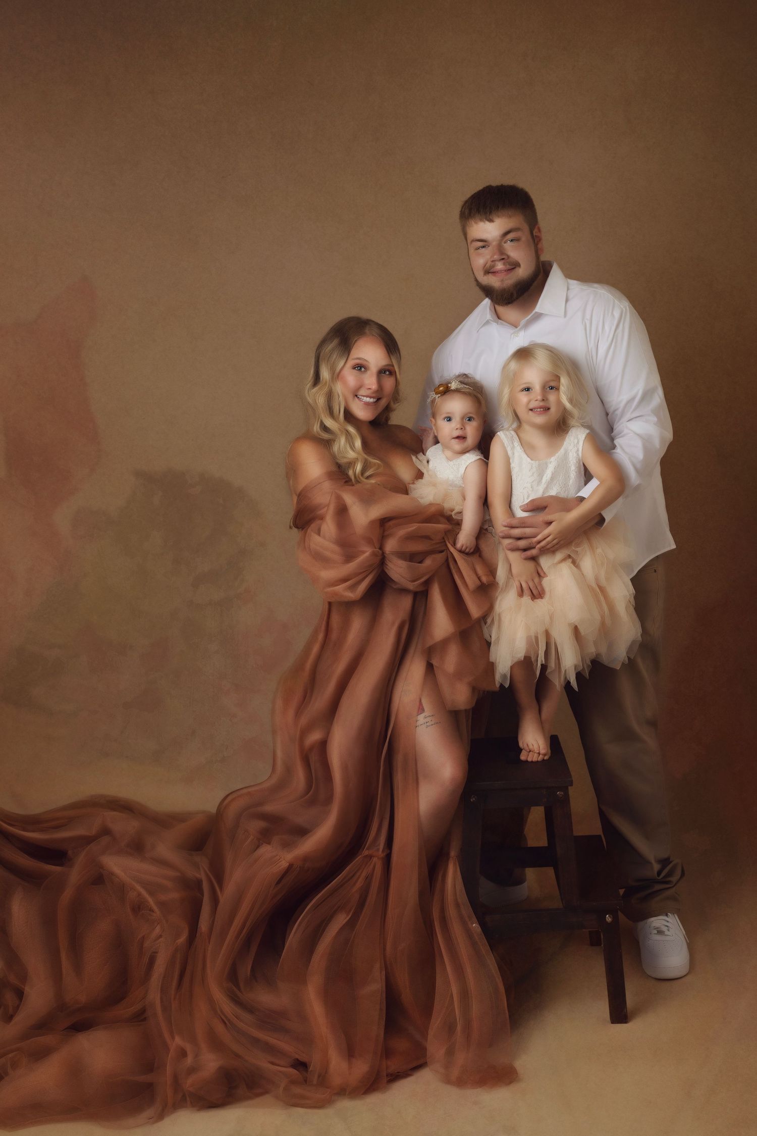 Family photoshoot featuring flowing brown dress against neutral backdrop in artistic poses.