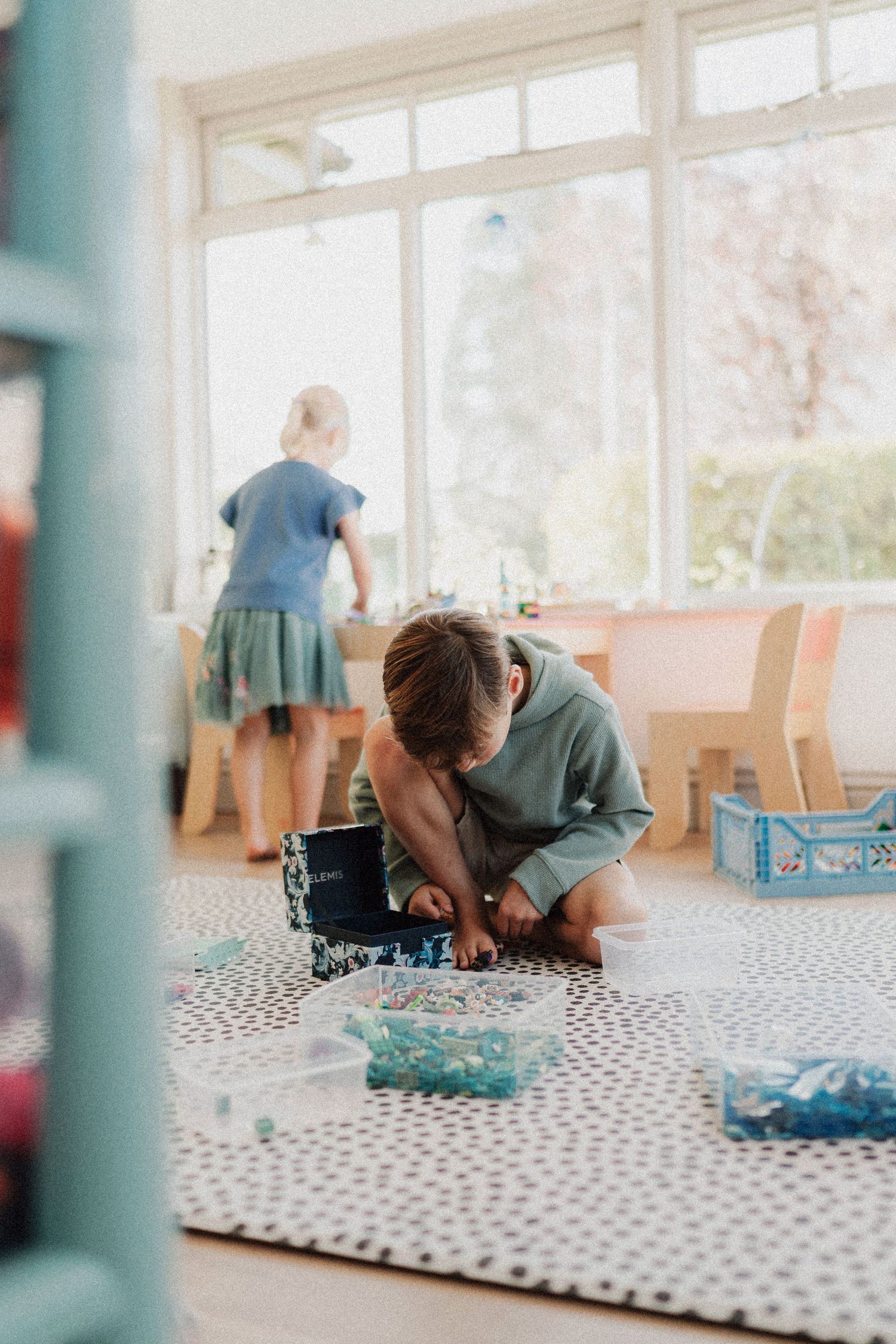 Child playing with toys on polka dot mat in bright sunlit room.