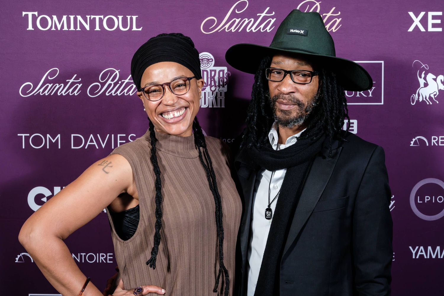 Two attendees pose together at a formal event with a purple branded backdrop.